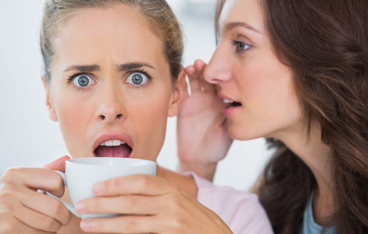 Woman telling secret to her friend and astonishing her while drinking coffee